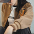 Person wearing a brown letterman jacket with a logo, sitting against a neutral background.